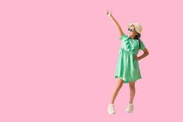 Happy smiling asian little girl were hat and sunglasses hands pointing space, Full body isolated on pink  background