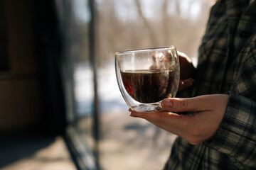 Closeup cropped shot of unrecognizable woman holding cup with hot aroma coffee in morning sunlight. Closeup of lady enjoying drinking coffee at home. Happy relaxed female drinking tea on kitchen.