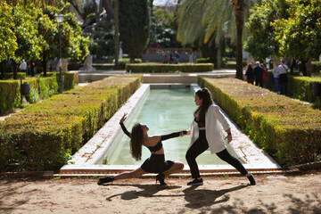 Couple of Latin women, young, dancing bachata with a beautiful fountain in the background in an...
