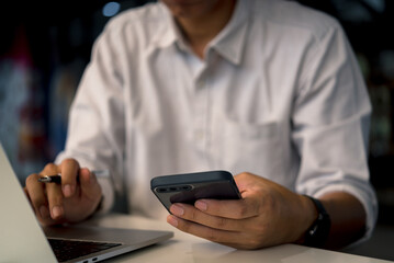 Businessman holding smartphone to communicate work with digital internet, online technology and laptop computer at work desk