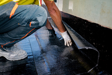 Worker unroll foil with bitumen waterproofing installation over concrete