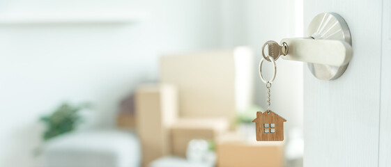 Fototapeta premium Moving house, relocation. The key was inserted into the door of the new house, inside the room was a cardboard box containing personal belongings and furniture. move in the apartment or condominium