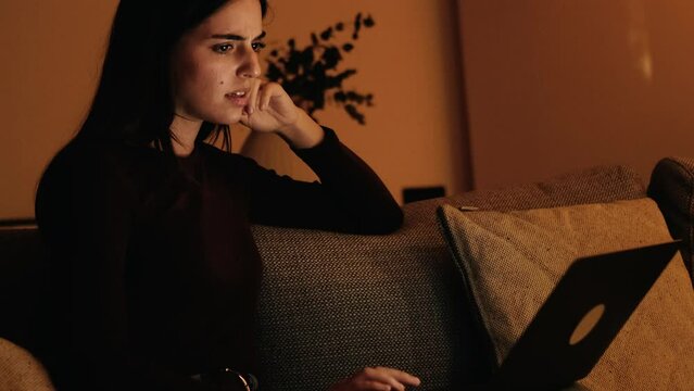 One adult woman using laptop by night indoor in living room sitting on sofa. Disappoint expression for fraud scam website. Error on computer during messaging. Bad notification, Insomnia lifestyle