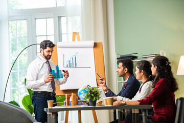 Confident Indian asian male or female boss or trainer make whiteboard presentation at team office...