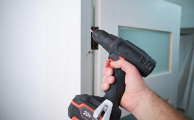 Construction worker holding electric cordless screwdriver in hand at construction site. Accessories for assembling, install furniture, repair home. Home renovation, electric tool for job. Crop view.