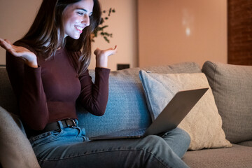 Obraz premium Happy brunette girl waving hand using laptop app enjoying online virtual chat video call in remote virtual meeting, relaxed and smiling talking in night with friends.