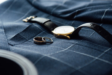Groom's wedding details. Watch, rings and belt placed on a checkered jacket