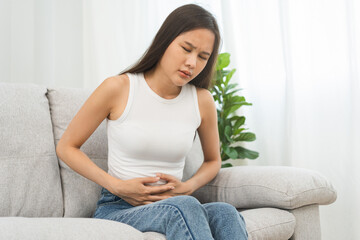 Obraz premium Flatulence asian young woman, girl hand in stomach ache, suffer from food poisoning, abdominal pain and colon problem, gastritis or diarrhoea. Patient belly, abdomen or inflammation, concept.