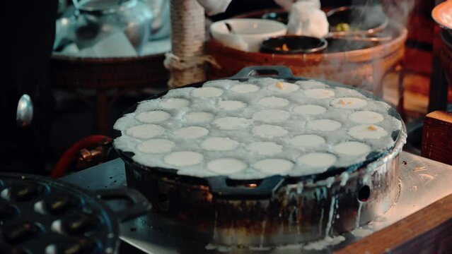 4K Close-up of woman's hand cooking traditional Thai street food coconut-rice pancakes.Khanom Khrok  is a traditional Thai dessert.