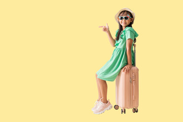 Happy smiling asian little girl were hat and sunglasses posing pointing with suitcase, Travel fashion summer holiday concept, Full body isolated on yellow background