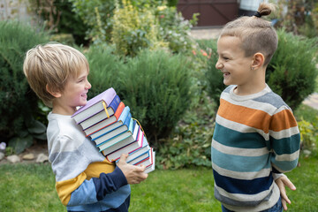 Two boys, classmates, friends are standing opposite each other, one child is holding a large stack...