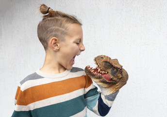 child plays with scary toy head of dinosaur, putting it on hand, scaring it with terrible grimace....