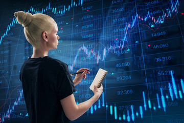 Side view of attractive young blonde european woman writing in notepad with creative candlestick forex chart with index on blurry office background. Trade and stock exchange concept. Double exposure.