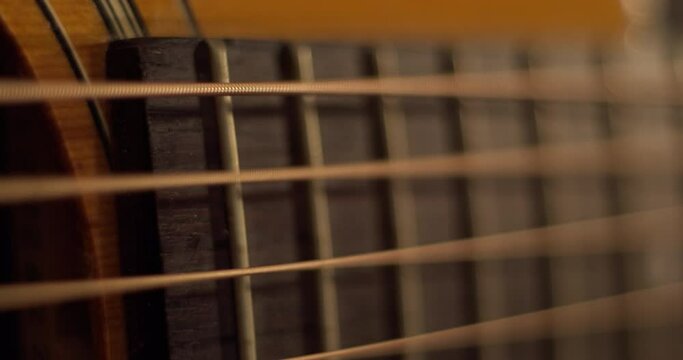 Extreme closeup on acoustic guitar fretboard and soundhole. Strings vibrating as chords are strum