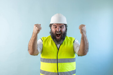 euphoric adult man engineer with beard and wearing helmet and safety vest, with raised fists,...