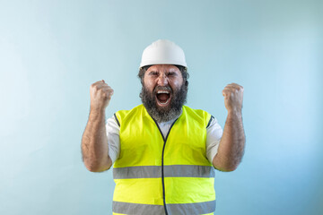 euphoric adult man engineer with beard and wearing helmet and safety vest, with raised fists,...