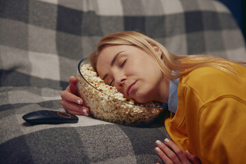 Sleepy woman is resting holding her head in plate with popcorn