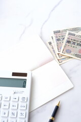 テーブルの上に開いた状態で置かれた銀行の預金通帳と、1万円札、電卓
