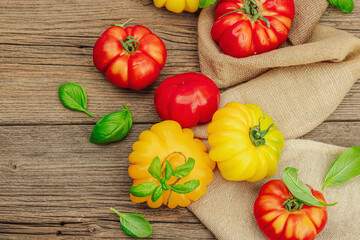 Colorful Heirloom tomato harvest. Ripe ribbed vegetables with fresh basil leaves. Wooden background
