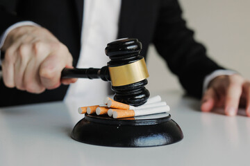 Judge hitting cigarettes with referee's gavel on white table. Tobacco law.