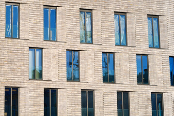 Row of floor-to-ceiling glass windows in modern building with clinker brick facade, showcasing the architectural design that allows for an abundance of natural light and expansive views of cityscape