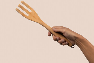 Hand holding wooden cooking fork on beige background