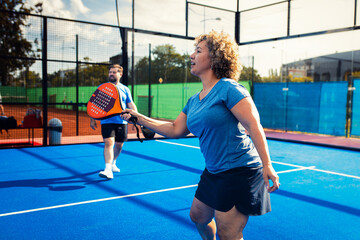 Mixed adult couple palying padel on outdoor court.
