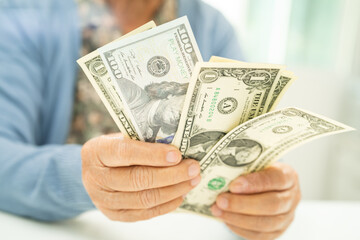 Asian senior woman holding and counting US dollar banknotes money in purse. Poverty, saving problem...