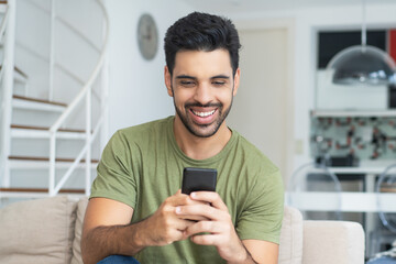 Laughing latin american man with fashionable beard shopping online with cellphone