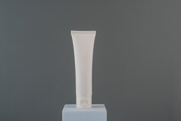 Plastic white tube for cream or lotion. Skin care or sunscreen cosmetic with stylish props on grey background.