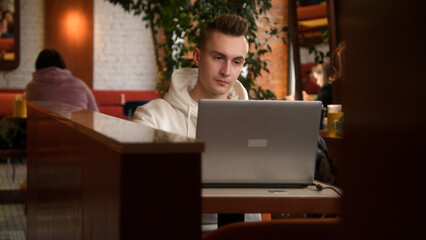 Tired young man is working on laptop in cafe. Stock footage. Handsome young man is writing diploma...