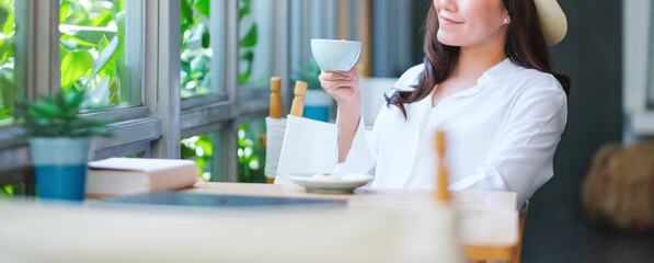 Closeup image of a young woman with hat drinking coffee and relaxing in cafe