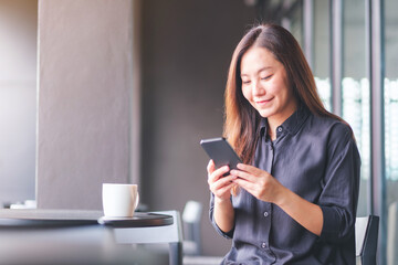 Portrait image of a young woman holding and using mobile phone in cafe - Powered by Adobe