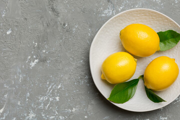 Fresh cutted lemon and whole lemons over round plate on colored background. Food and drink ingredients preparing. healthy eating theme top view vith copy space