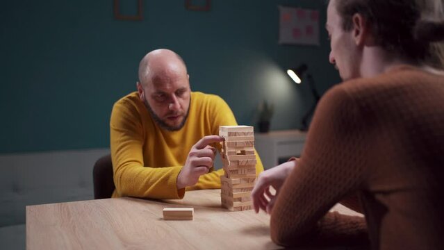 Two friends are deeply engaged in a game of Jenga in a comfortable indoor environment, carefully focusing on each move