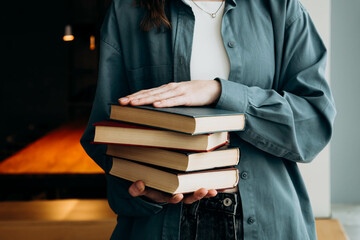 A woman in a blue shirt holds a stack of books on a dark library background.