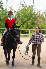 Instructor leads young rider on horse in training session.