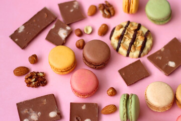 Pastel macarons, almond chocolate, peanut butter cookies and various nuts on bright pink background. Selective focus.