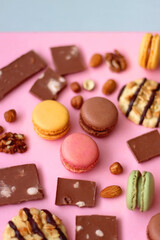 Pastel macarons, almond chocolate, peanut butter cookies and various nuts on bright pink background. Selective focus.