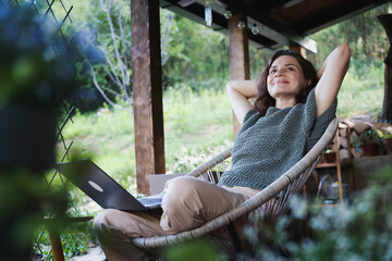 Young happy smiling Caucasian woman sitting on the terrace in an armchair enjoying country lifestyle