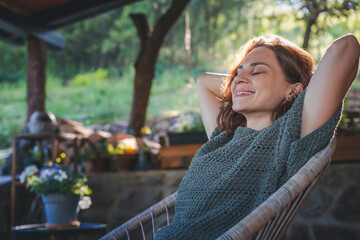 Young happy smiling Caucasian woman sitting on the terrace in an armchair enjoying country lifestyle