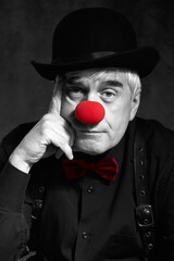 Dramatic selective color portrait of a sad clown against a dark background. Hand near face.