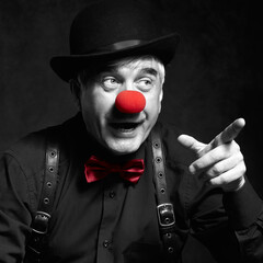 Selective color portrait of laughing clown. Dressed in black shirt with suspenders, red clown nose...