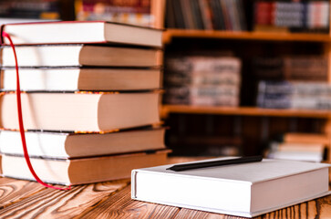 A white notebook and a black pencil on the desktop with bookshelves in the background. Books