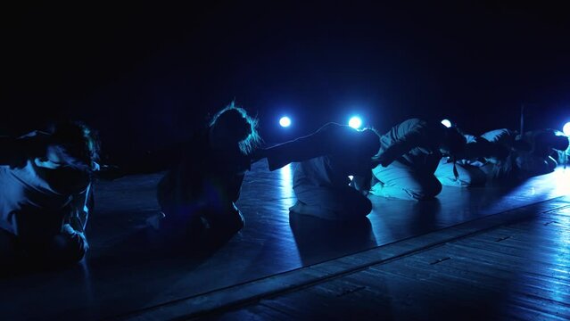 A group of girls performing on stage. A girl sits on an illuminated stage with smoke and performs a performance.