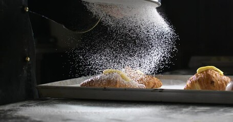 Super slow motion macro of professional artisan baker chef sprinkles sugar icing powder with sieve on homemade pastries sweet delicious dessert French croissants dessert in traditional bakery kitchen.