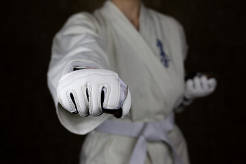 Young woman in kimono and white belt throws punch in protective gloves in Kyokushin karate to...