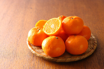 ザルに盛った丸ごとみかんと断面　木目背景