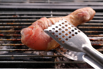 Metal tongues holding grilled sausage in front of bbq grill close up