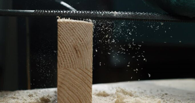 Super slow motion macro of artisan carpenter is working wood with hacksaw with flying wood sawdust on workbench in workshop at 1000 fps.